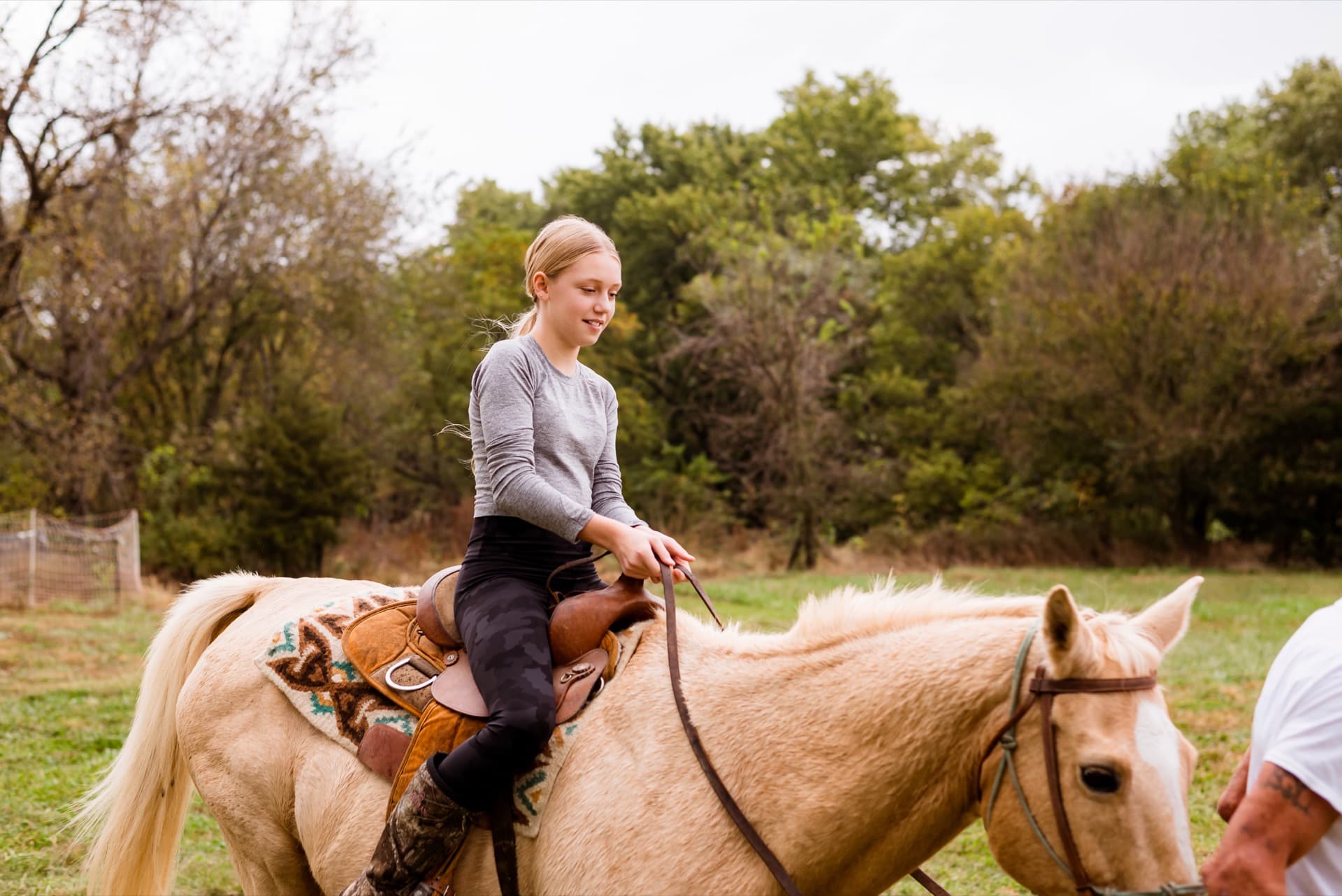 Girl riding a palomino horse through green pasture